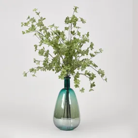 Green leafy branches in teal glass bottle vase